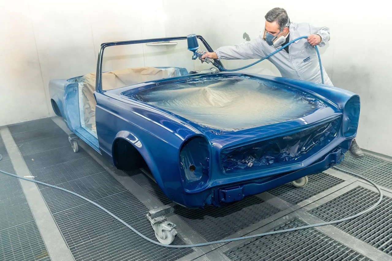 Spray painter refinishing a car body in a spray booth